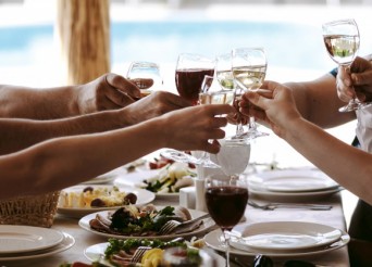 Table de restaurant avec des mains qui trinque avec des verres remplis.