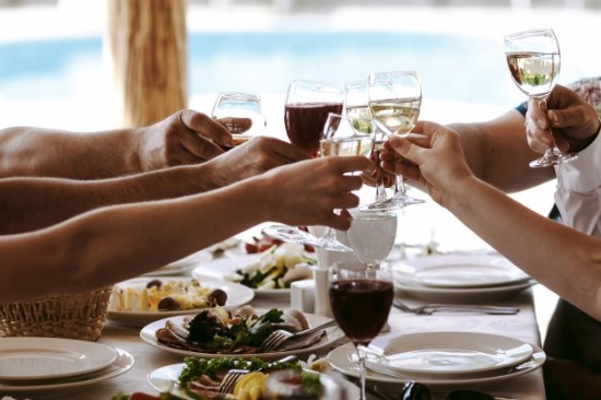 Table de restaurant avec des mains qui trinque avec des verres remplis.