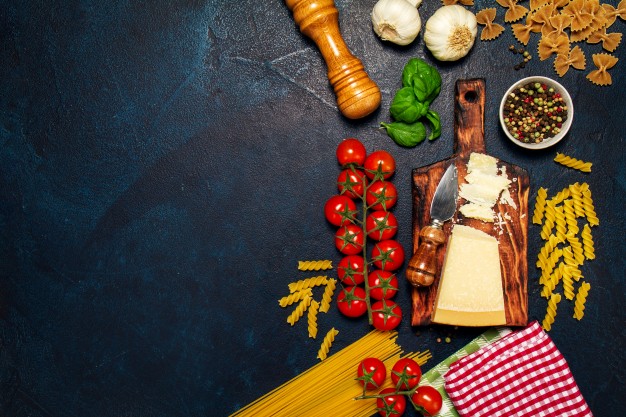 Table sombre, avec des aliments éparpillées tels que des pâtes, des tomates, des épices etc...